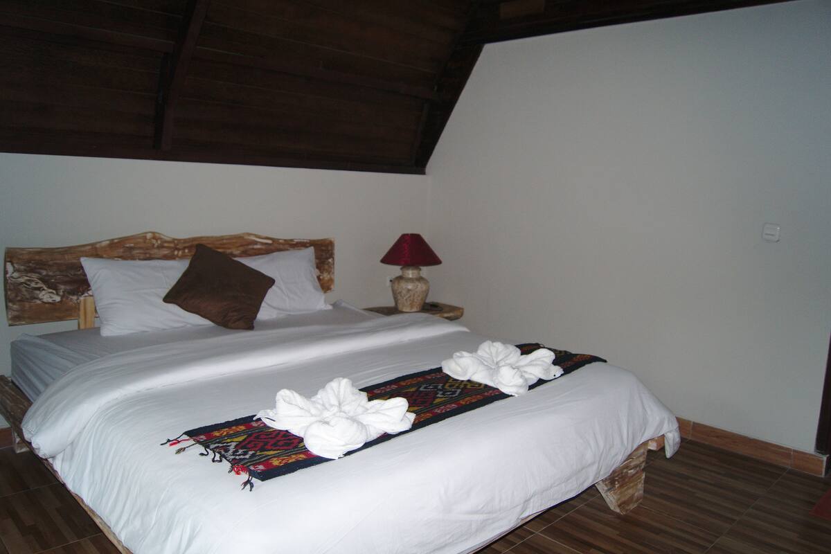 A neatly made bed with white linens, a decorative headboard, and a red lamp on a wooden nightstand.
