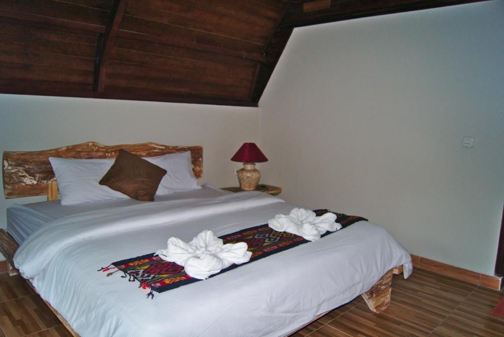 Una cama individual con sábanas blancas, un cabecero de madera, una lámpara roja sobre una mesita de noche y un cojín decorativo.