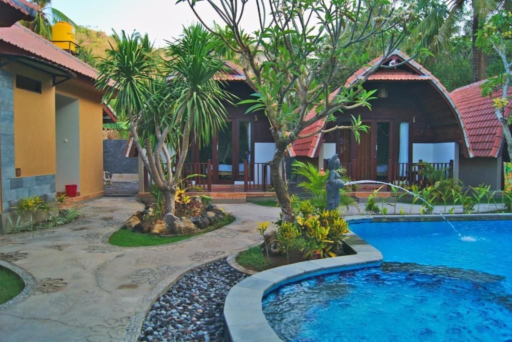 A pool area with a curved edge, surrounded by a garden with palm trees and a small pond.
