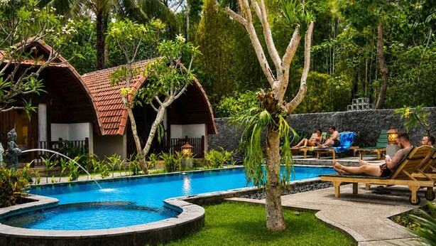 Un área de piscina con sillas de descanso, una pequeña cascada y vegetación tropical.
