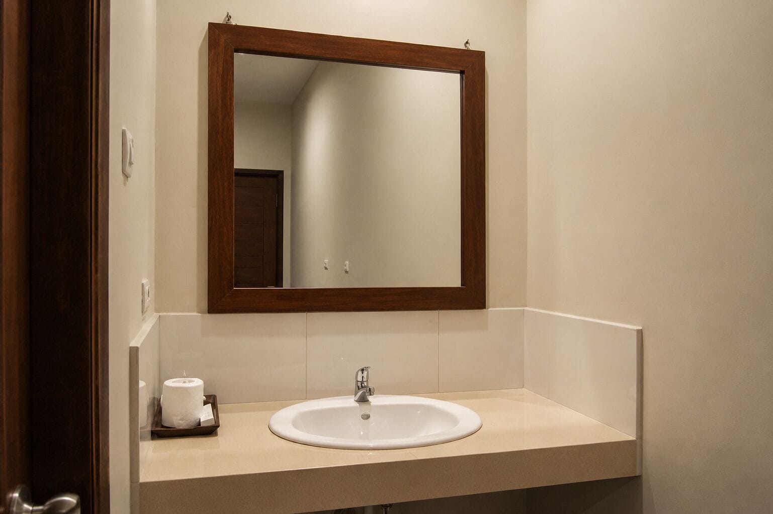 A bathroom with a white sink, a mirror with a wooden frame, and a toilet paper holder.