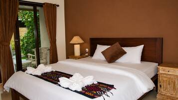 A hotel room with a large bed, a nightstand with a lamp, and a view through a glass door.
