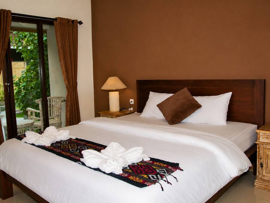 A hotel room with a large bed, a nightstand with a lamp, and a view through a glass door.