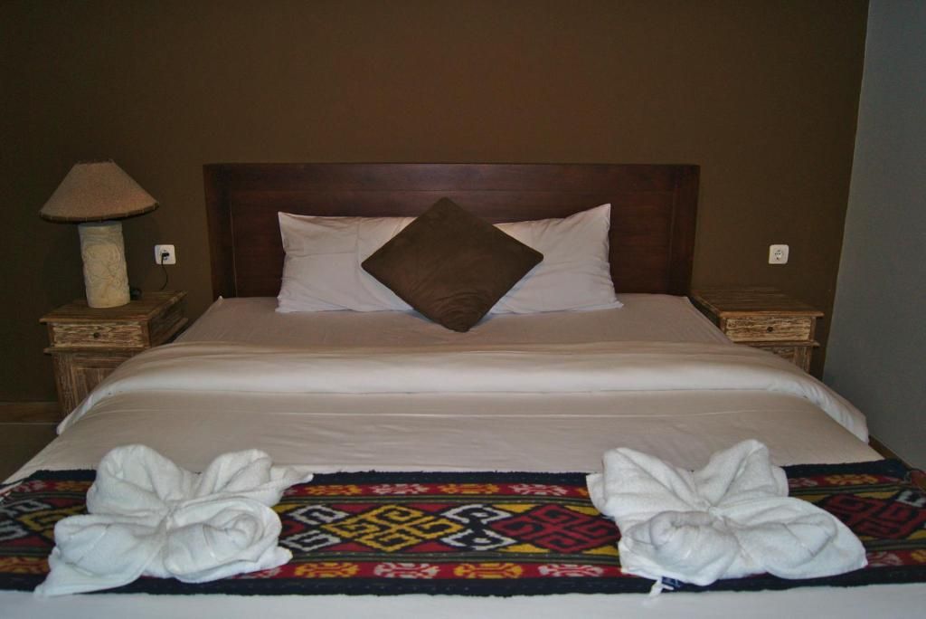 A neatly made bed with a patterned rug and two towels.