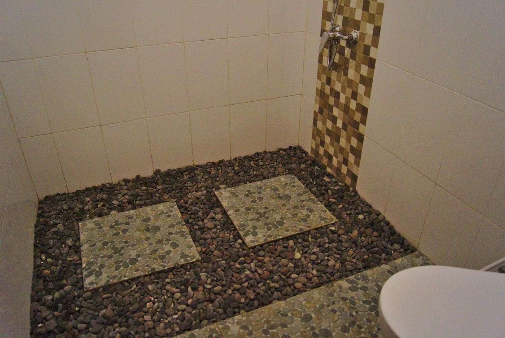 A shower area with tiled walls, a checkered tile accent wall, and a pebble-tiled floor.