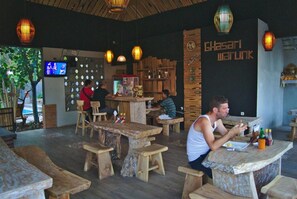 A restaurant interior with wooden tables and benches, a TV screen, and a wall with a sign. - Ghamed Sari (Karangasem)