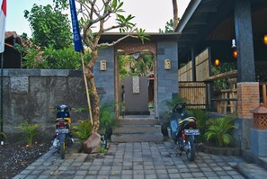 A gated entrance with a sign, two motorcycles parked outside, and a pathway leading to a building. - Ghamed Sari (Karangasem)
