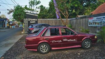 A maroon car parked on a gravel surface with a sign in the background.