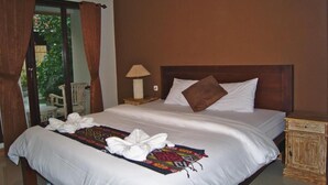 Habitación de hotel con una cama grande, una mesita de noche, una lámpara y vistas al exterior.
