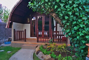 A covered outdoor area with a wooden fence, a stone wall, and a variety of plants. - Ghamed Sari (Karangasem)