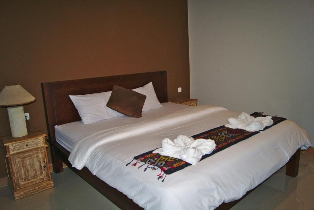 Una cama bien hecha con ropa de cama blanca, una almohada marrón y una toalla decorativa sobre el edredón.
