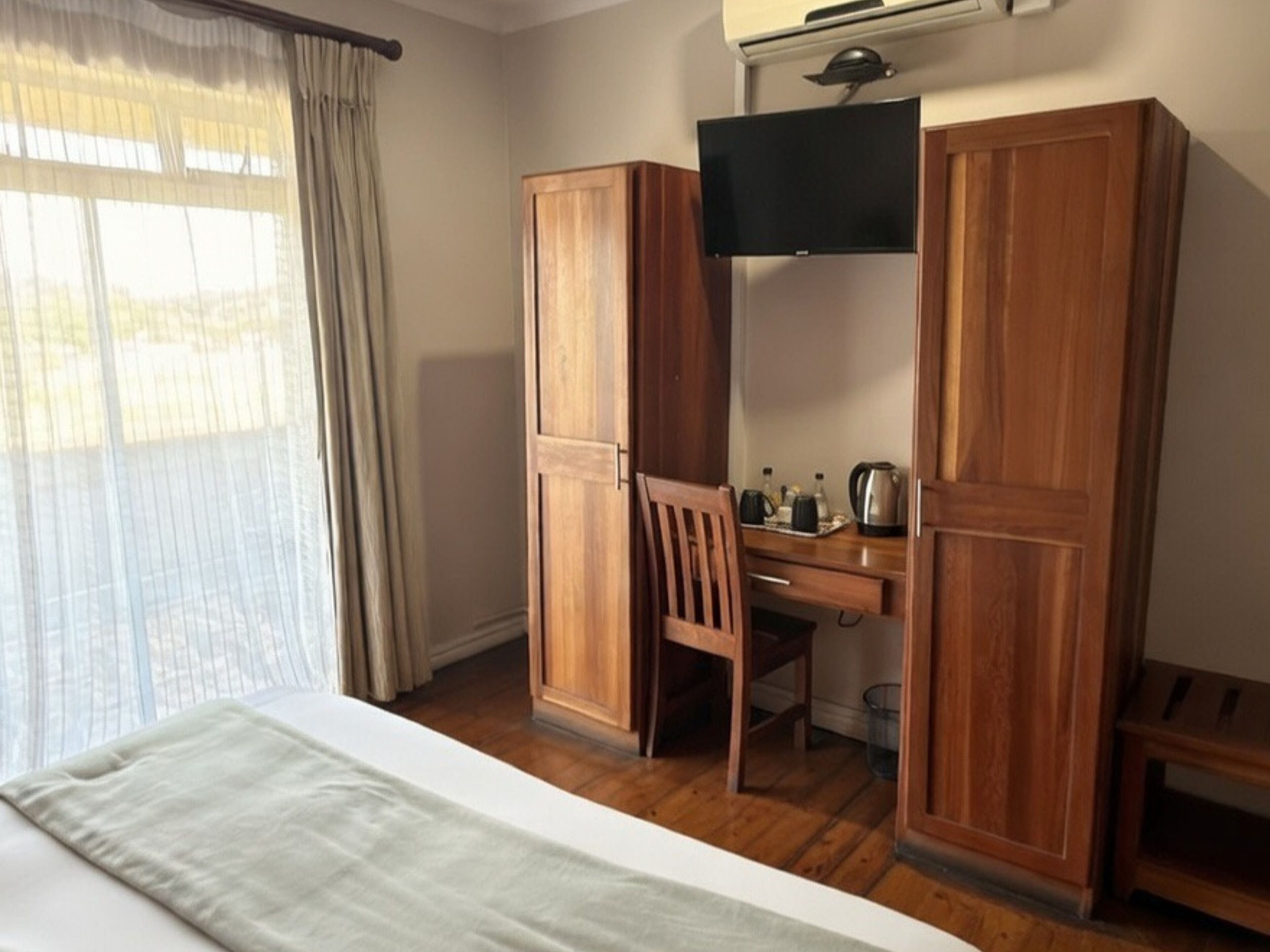 Una habitación de hotel con cama, armario de madera, escritorio, silla y televisión.