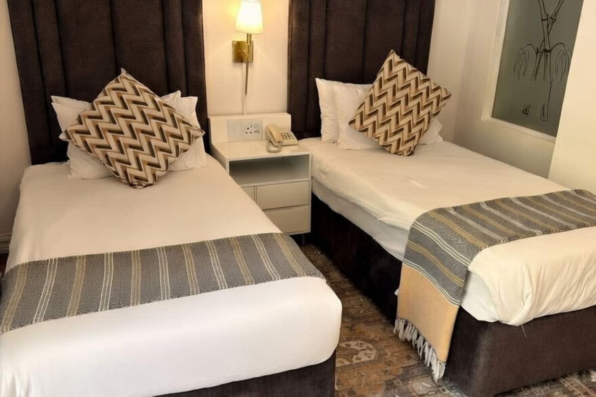 Ein Hotelzimmer mit zwei Betten, einem Nachttisch, einer Lampe und einem Wandbild.