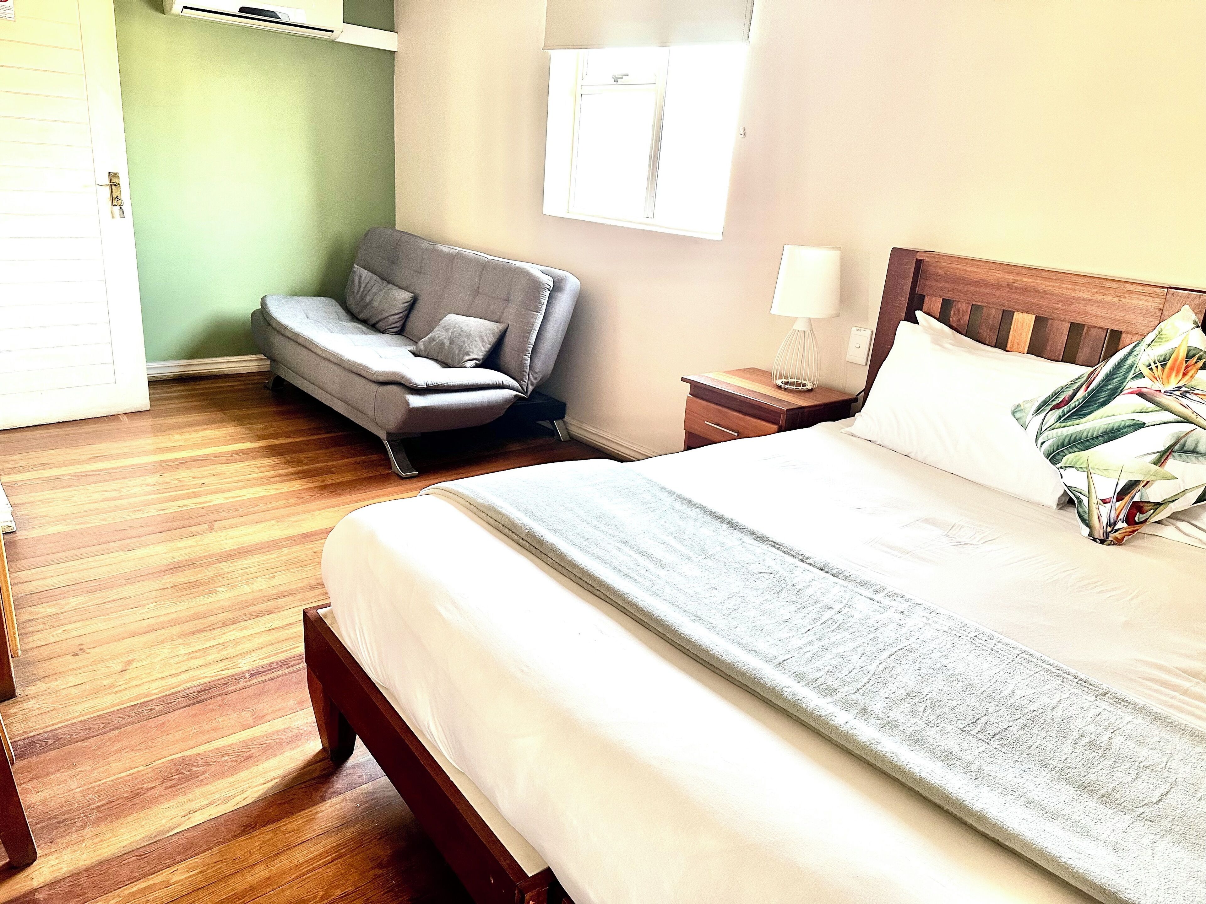 Quarto de hotel com cama, sofá, mesa de cabeceira, luminária e janela.