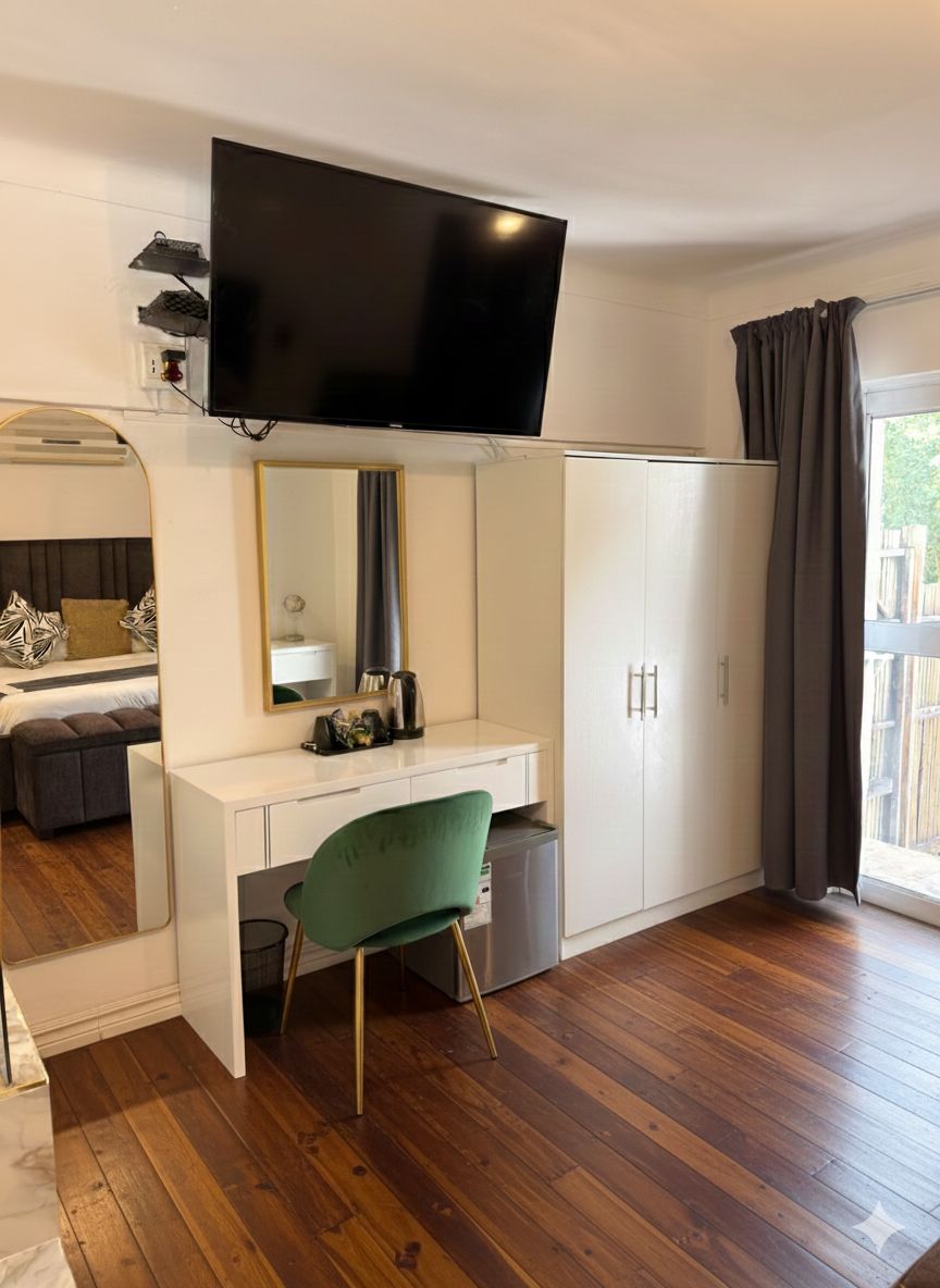 A modern room with a flat-screen TV mounted above a white desk, a green chair, and a wardrobe.