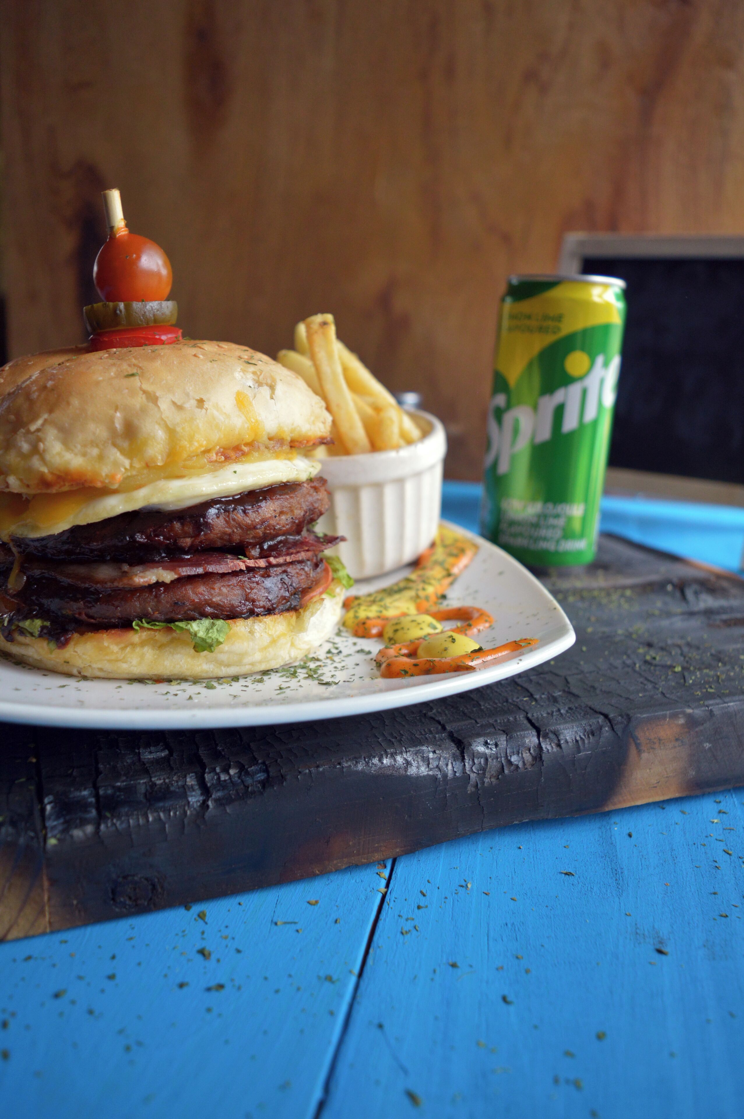 Un hamburger accompagné de frites et d’une canette de Sprite, le tout posé sur une table en bois.