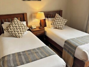 Une chambre d’hôtel avec deux lits, chacun agrémenté d’un oreiller à motifs et d’une table de chevet avec une lampe.