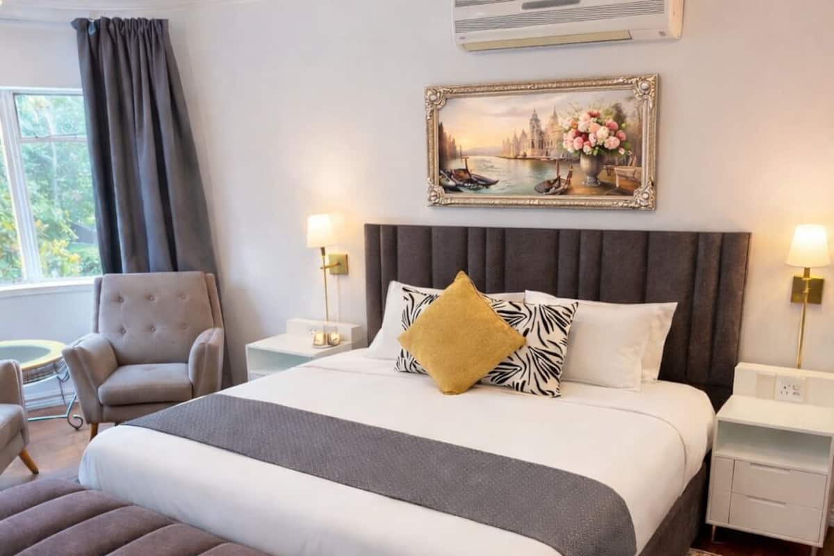 Ein modernes Schlafzimmer mit einem großen Bett, einer grauen Sitzbank, einem gemusterten Teppich und einem gerahmten Bild an der Wand.