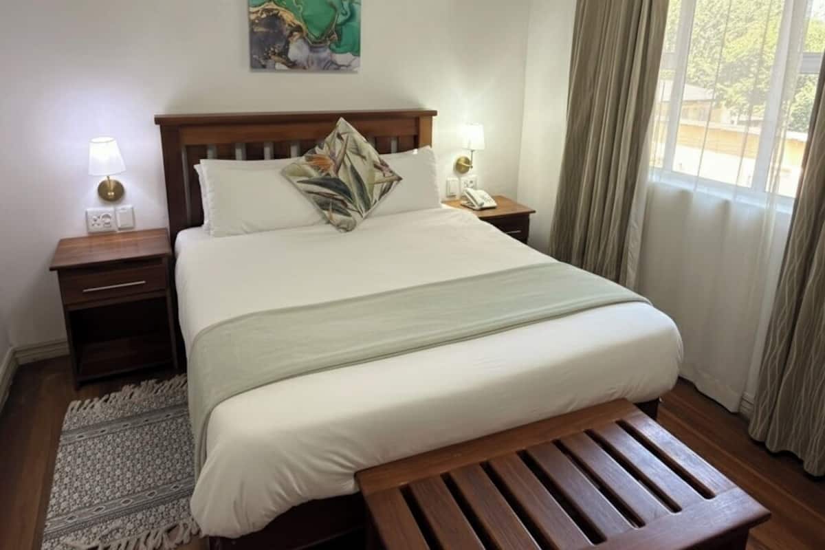 Ein ordentlich eingerichtetes Schlafzimmer mit einem großen Bett, Nachttischlampen, einem kleinen Tisch und einem Fenster mit Vorhängen.