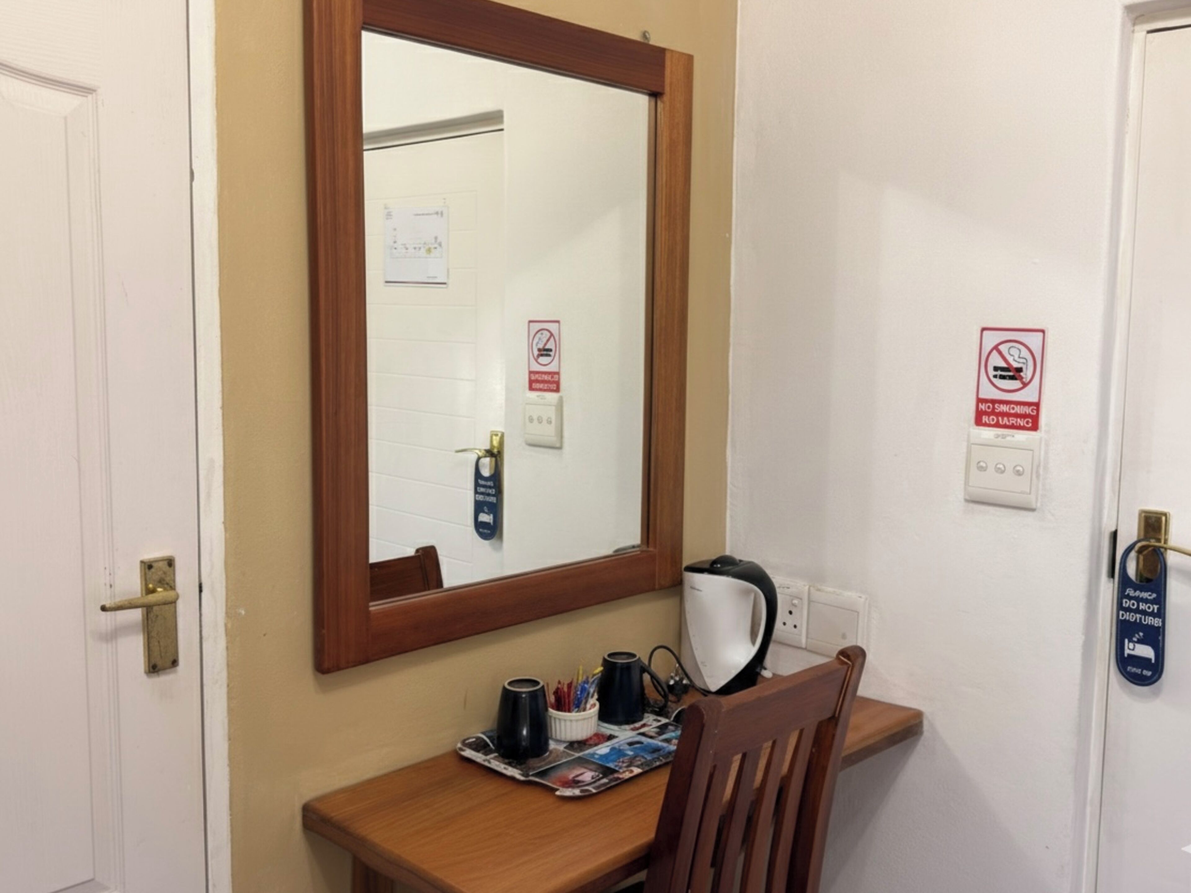 Una habitación pequeña con un escritorio de madera, un espejo y una silla. Hay letreros en la pared que indican prohibido fumar y prohibido el ralentí.