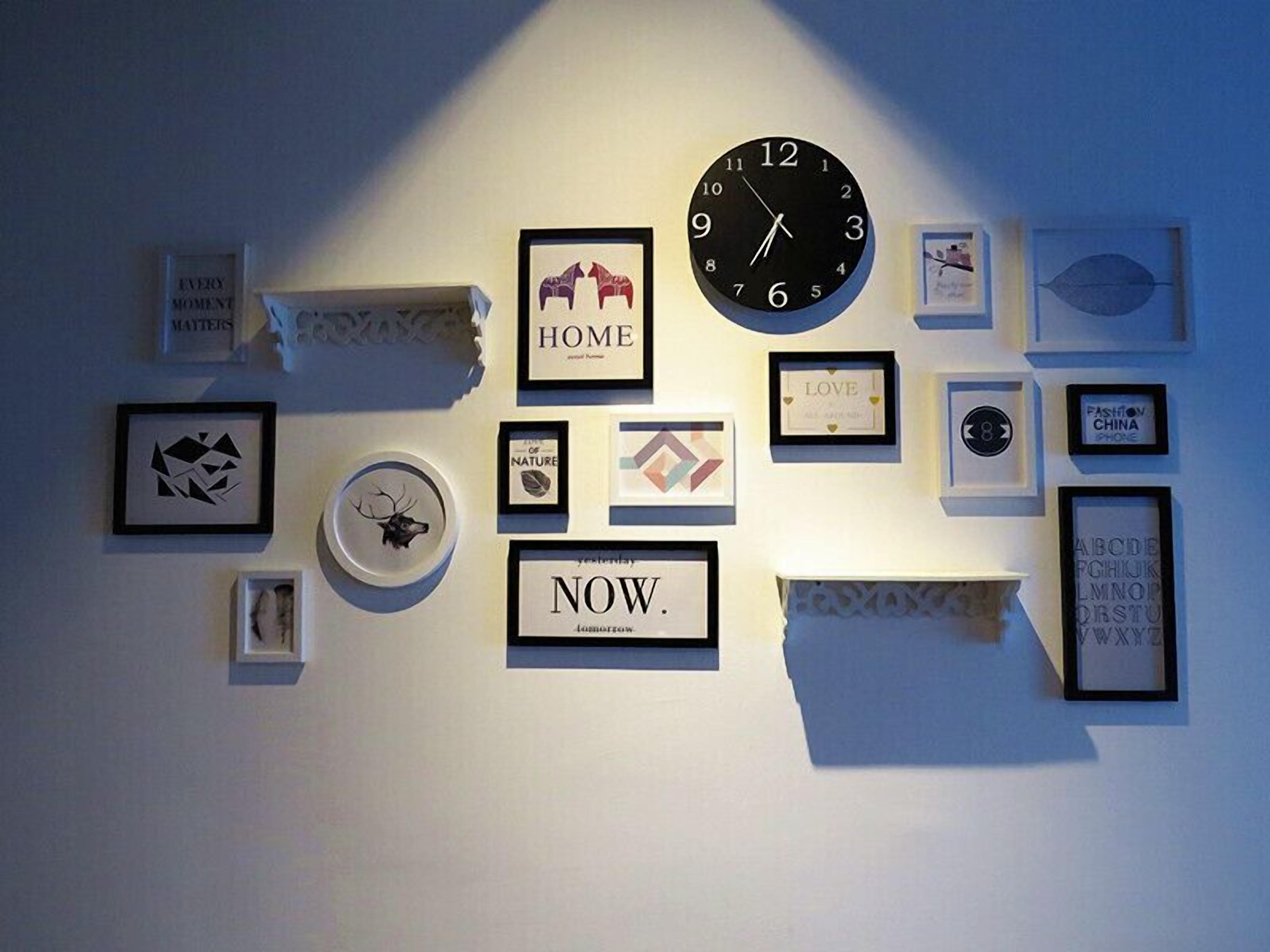 Pared amb diversos objectes emmarcados, com un rellotge, text emmarcat i art abstracte.