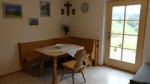 Un coin repas avec une table et un banc en bois, une plante en pot et une vue à travers une porte vitrée.