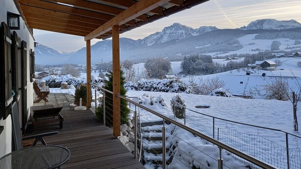Une terrasse en bois offrant une vue sur des montagnes enneigées et un village.