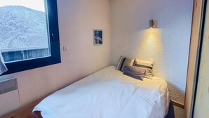Une petite chambre avec un lit simple, une fenêtre, une lampe fixée au mur et un petit tableau.