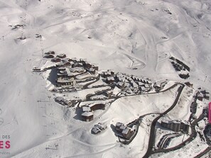 Eine Luftaufnahme eines schneebedeckten Skiortes mit mehreren Gebäuden, kurvenreichen Straßen und Skipisten.