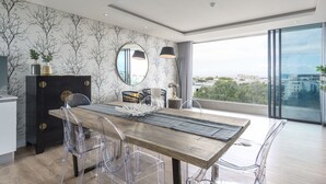 Ein moderner Essbereich mit einem Holztisch, transparenten Stühlen und Blick auf die Stadt durch große Fenster.