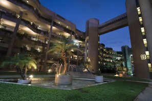 Un edificio de varios pisos con balcones, una fuente central y zonas exteriores bien iluminadas.