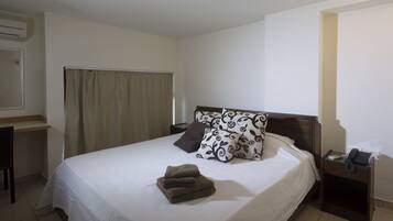 Una habitación de hotel con cama, escritorio, teléfono y aire acondicionado instalado en la pared.