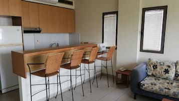 A compact kitchen with a central island, four bar stools, a small table, and a sofa with floral cushions.