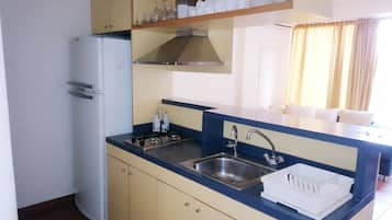 Cocina compacta con refrigerador, pileta y estufa. Hay gabinetes sobre la encimera y una ventana con cortinas.