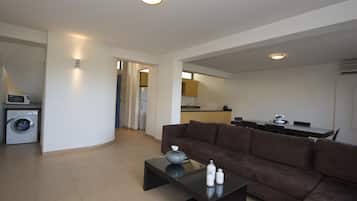A modern living room with a brown sofa, a glass coffee table, and a washing machine in the corner.