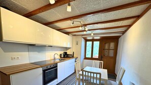Een kleine keuken met witte kastjes, een houten aanrechtblad, een inbouwoven en een eethoek met een tafel en stoelen.