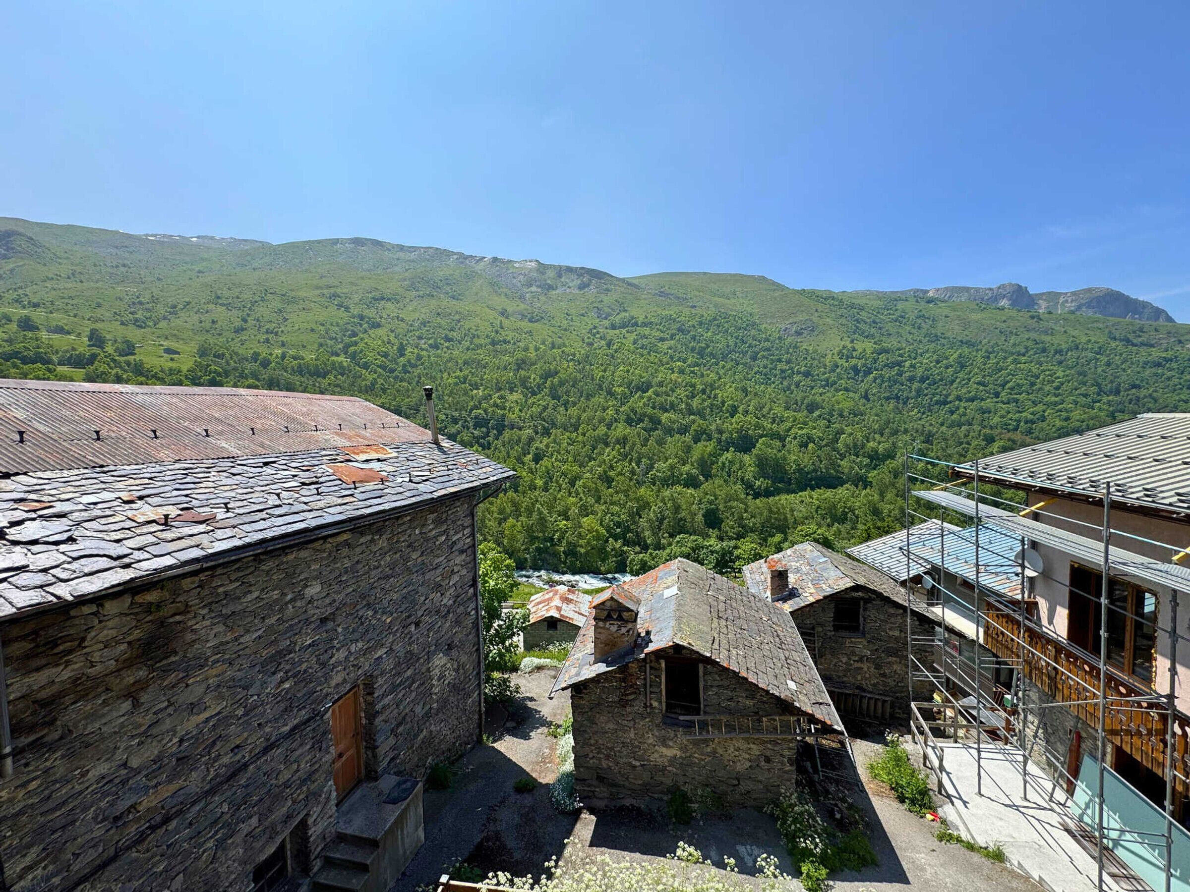 A stone building with a sloped roof, surrounded by lush green hills and a clear sky.