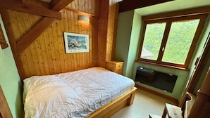 Een houten slaapkamer met een bed, een nachtkastje, een bankje en een raam met uitzicht op een bos.