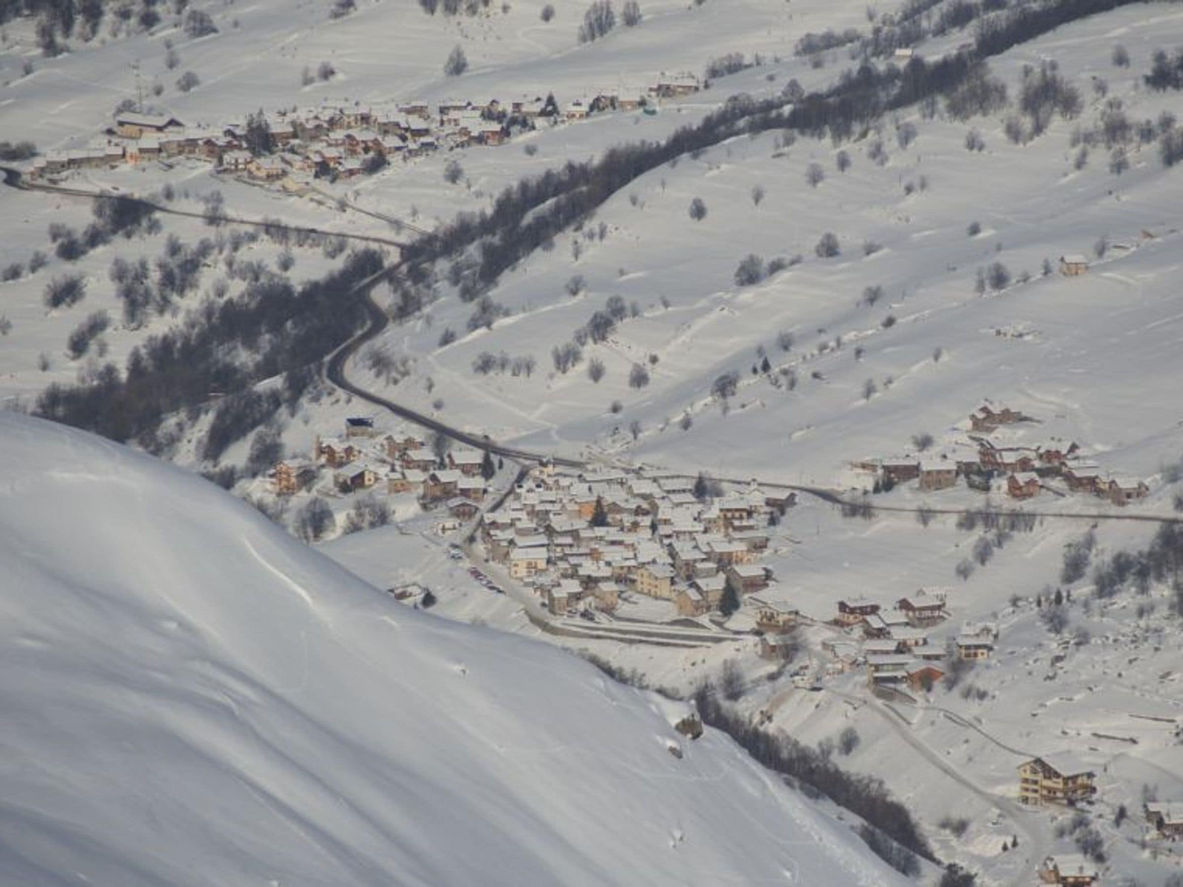 Un village enneigé où les bâtiments sont regroupés le long d’une route sinueuse.