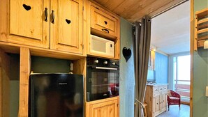 A compact kitchen with wooden cabinets, a black refrigerator, a microwave, and an oven.