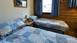 Et værelse med to senge, en trævæg, et vindue med gardiner og et billede i ramme på væggen.