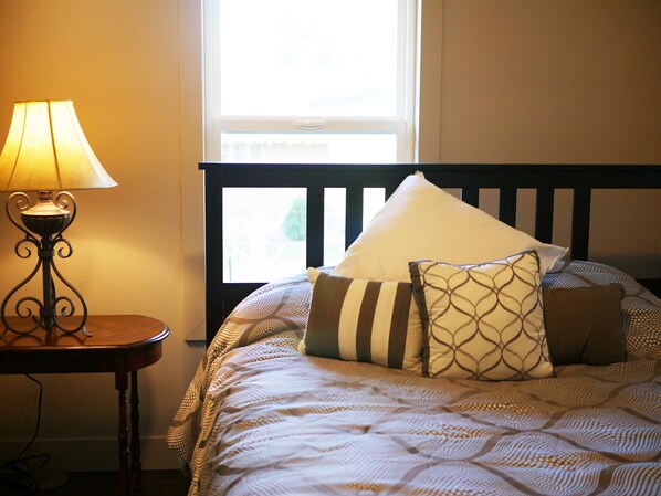 Een netjes opgemaakt bed met beddengoed met een patroon, een bedlampje en een raam met jaloezieën.