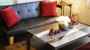 A modern living room with a black leather sofa, two red cushions, a wooden coffee table with decorative items including pinecones and flowers, and a vase with white flowers. - Quiet, Convenient Location w/ Great Amenities-Full Kitchen-Washer/Dryer-5g Wifi  (Hyrum)