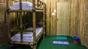 Habitación con literas, una pared de bambú y una colchoneta verde y otra azul en el suelo.