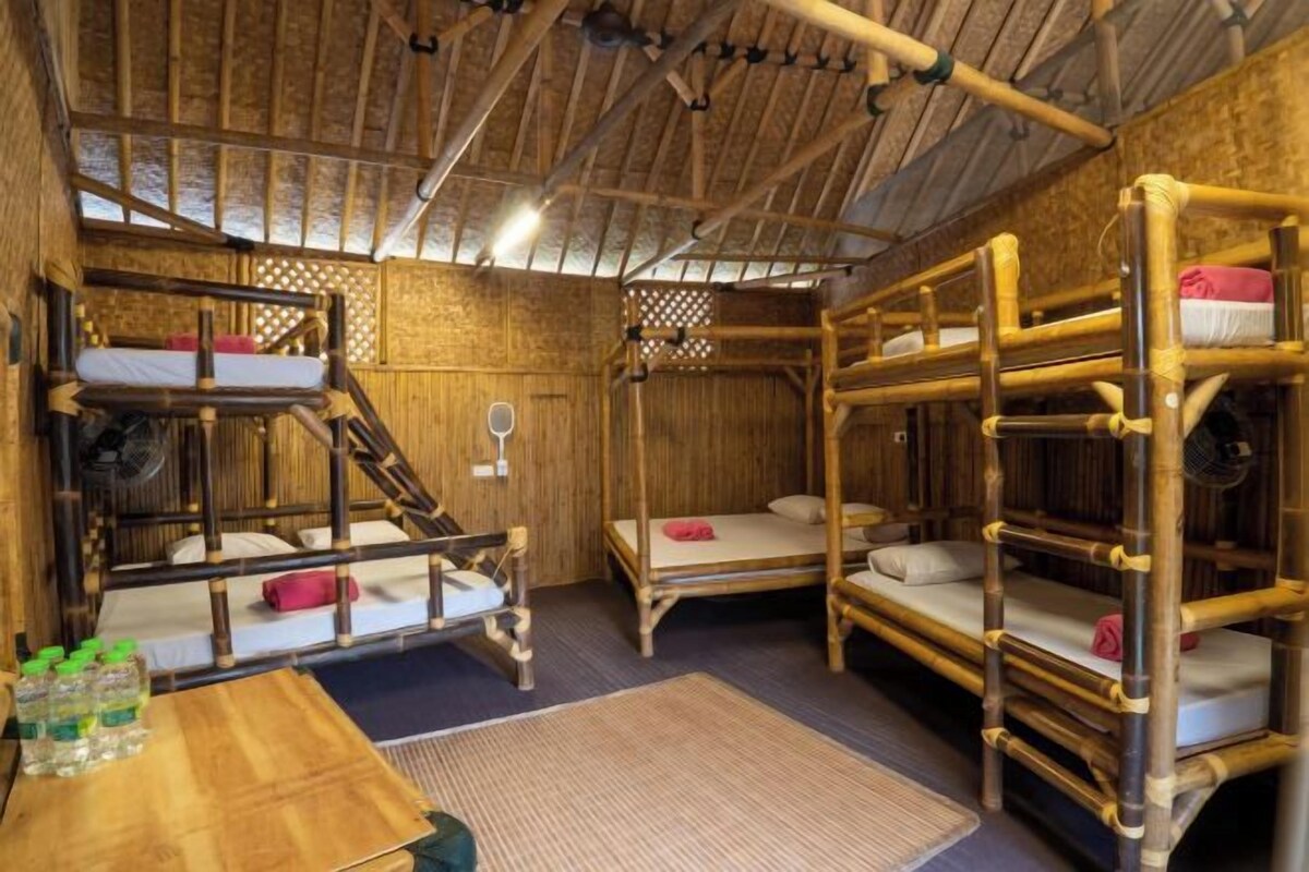 A room with bunk beds, a wooden table with water bottles, and a woven mat on the floor.