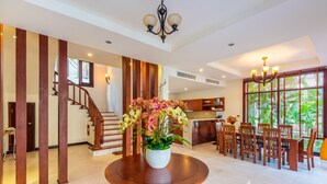 A spacious dining area with a round wooden table, a potted orchid centerpiece, and a staircase leading to an upper level.