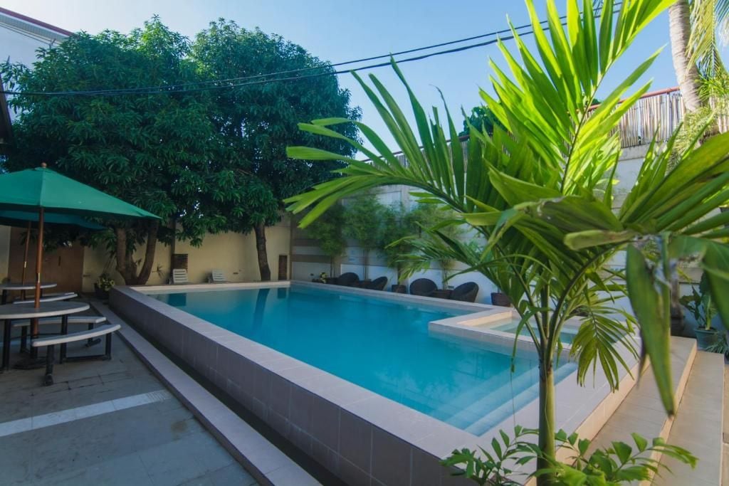 A swimming pool with a tiled edge, surrounded by greenery and a covered seating area.