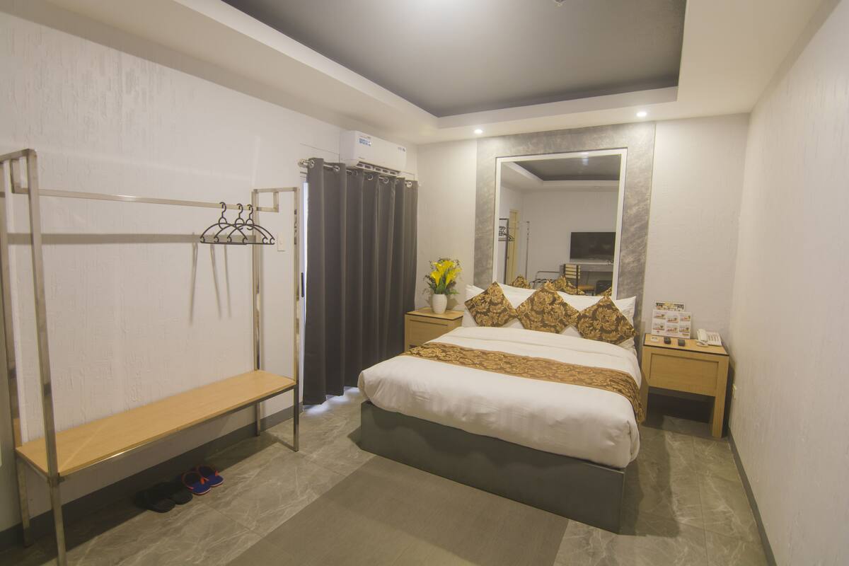 A bedroom with a bed, a bench, a mirror, a nightstand, and a wall-mounted coat rack.