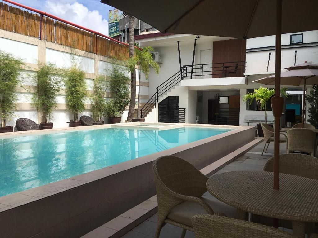 Una piscina con un patio circundante, que incluye mobiliario de mimbre y una escalera que conduce a un nivel superior.