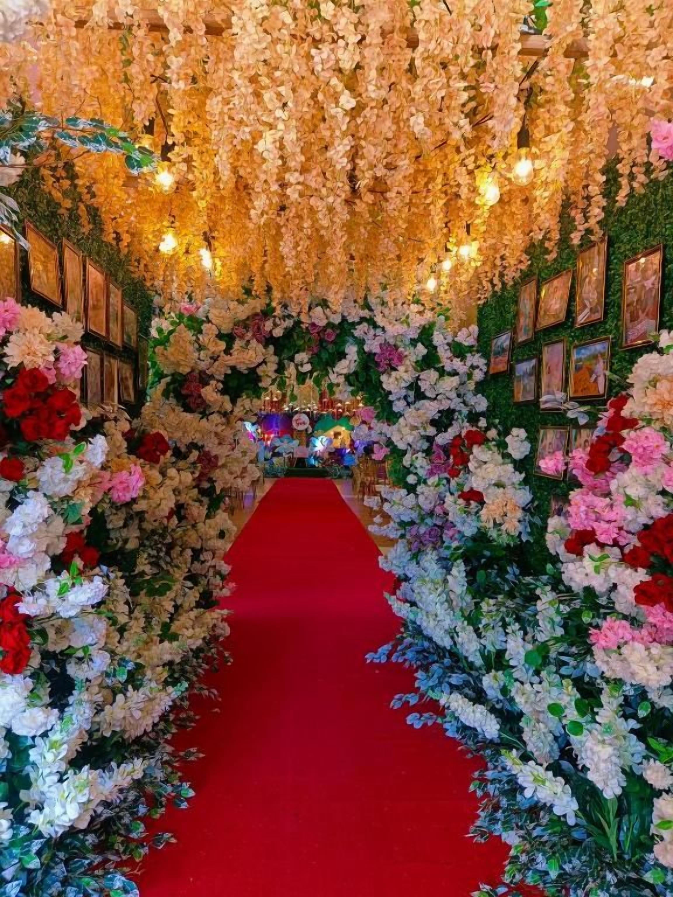 En rød løber fører gennem en blomsterpyntet portal med billeder i rammer på væggene.